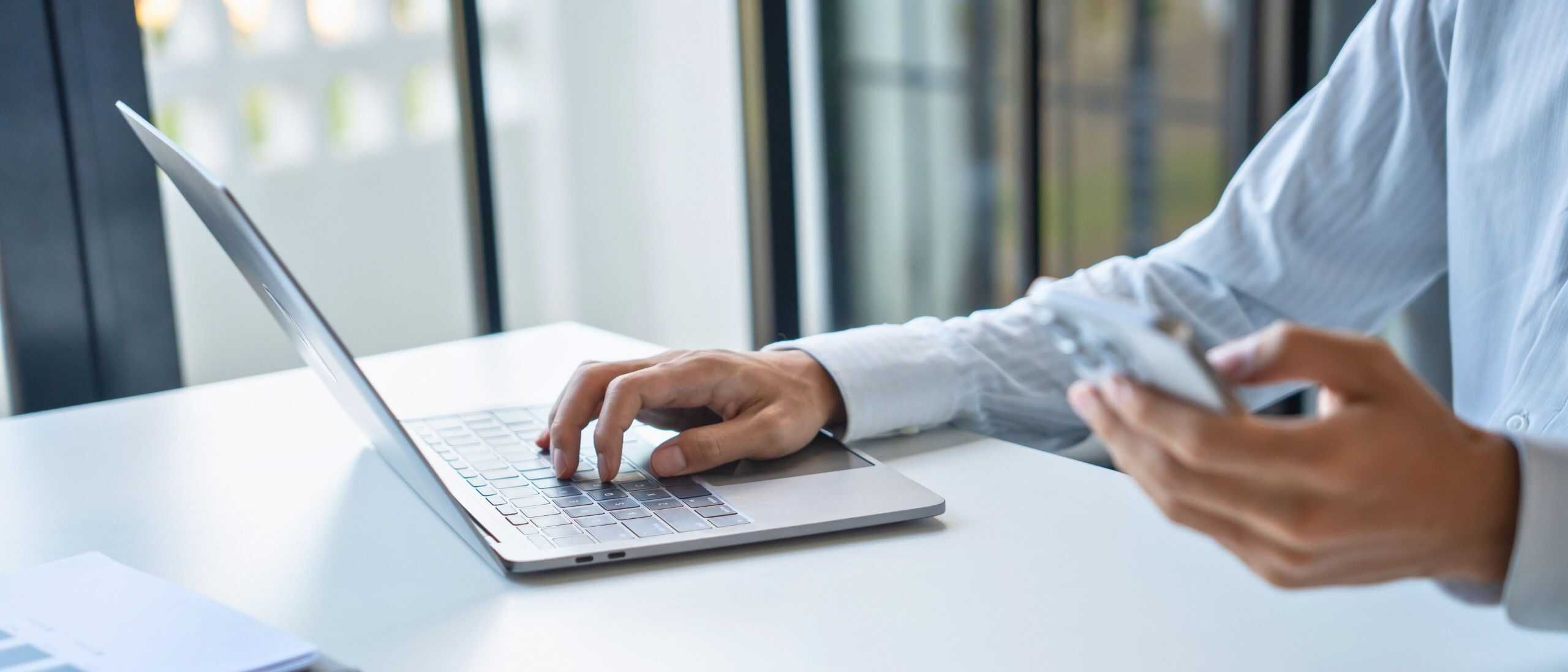 Modernes Business-Management, Person am Laptop und Smartphone im Büro, Produktivität und Digitalisierung.