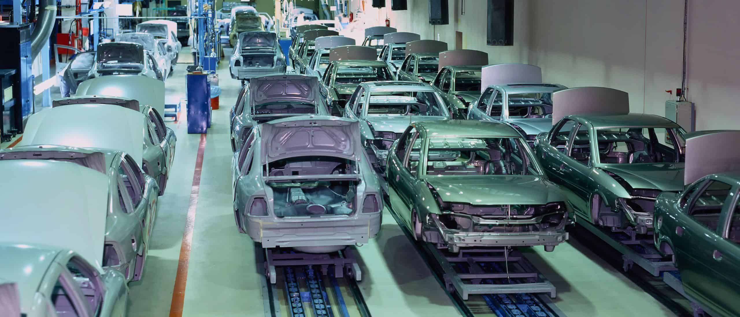 Fahrzeugmontage in einer modernen Automobilproduktion, mit zahlreichen Autokarosserien in verschiedenen Bauphasen, in einer großen, gut ausgestatteten Fabrikhalle.